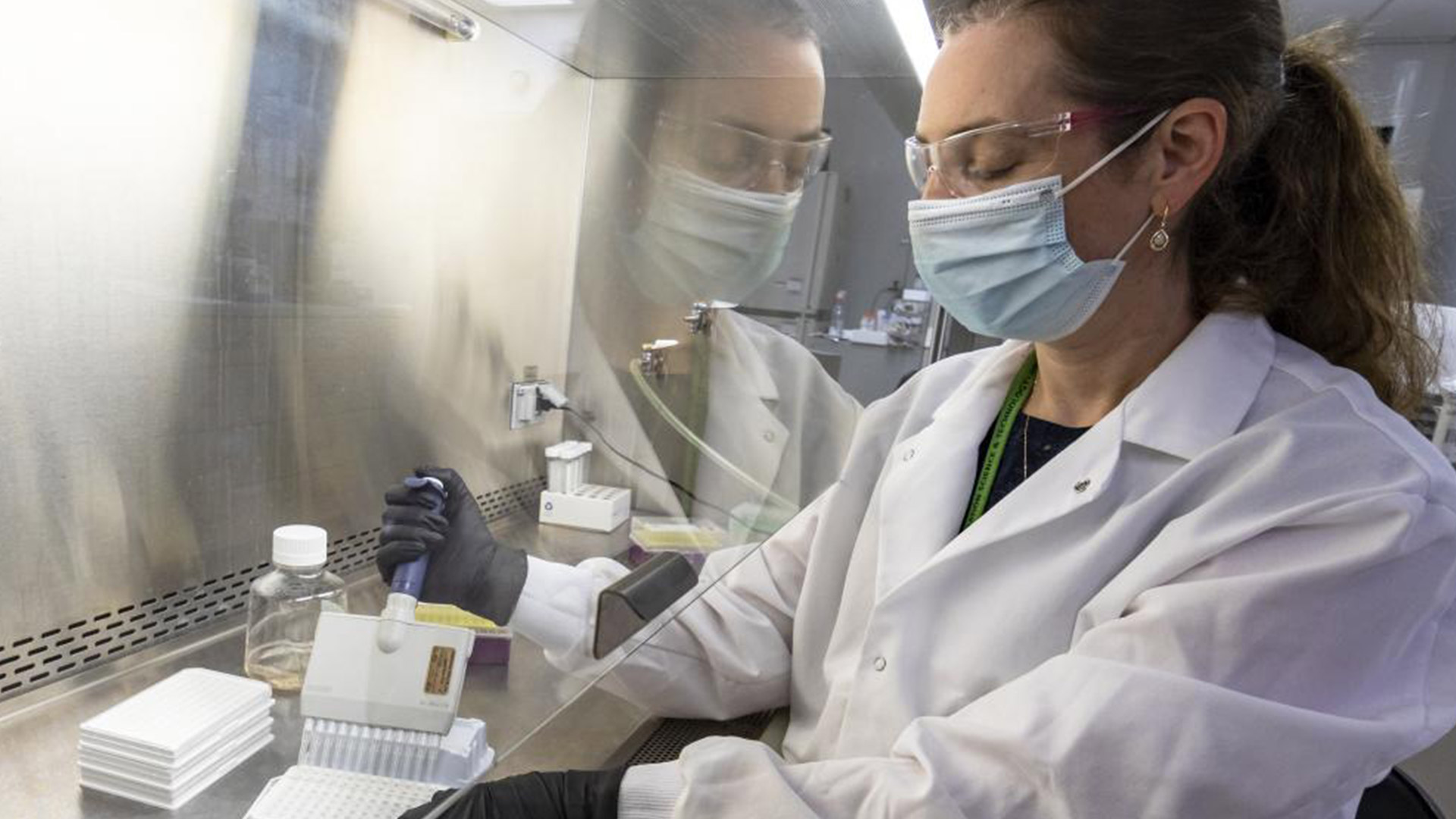 A white female scientist performs research behind a glass panel.