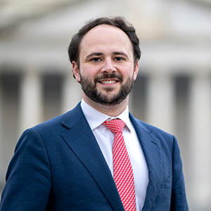 A white male in a business suit and red tie.