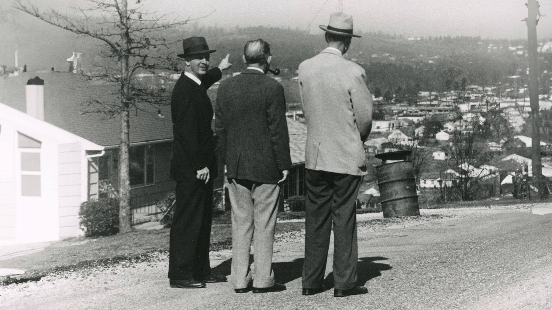 Old black and white photo from the late 1940s, showing three men suits overlooking a cityscape.