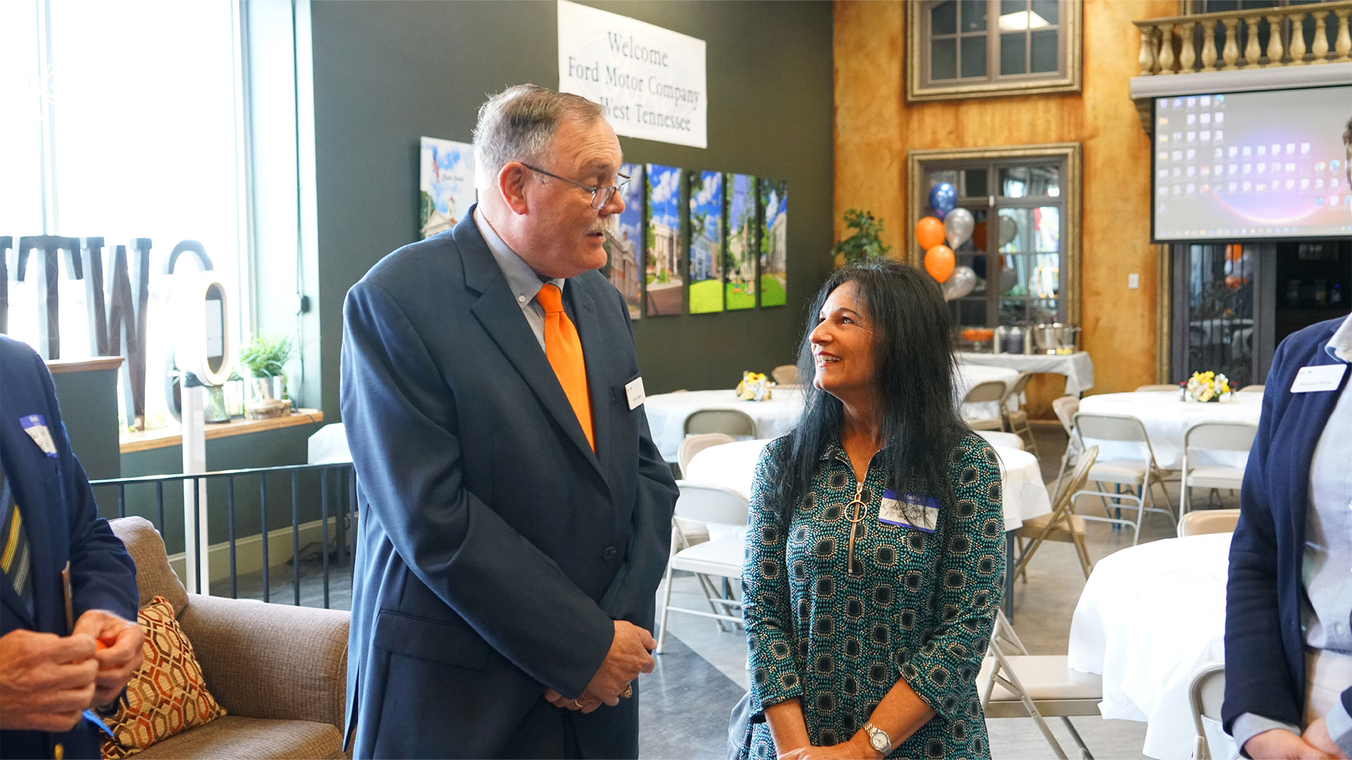 An elderly man in a suit talks with a woman in a green dress.