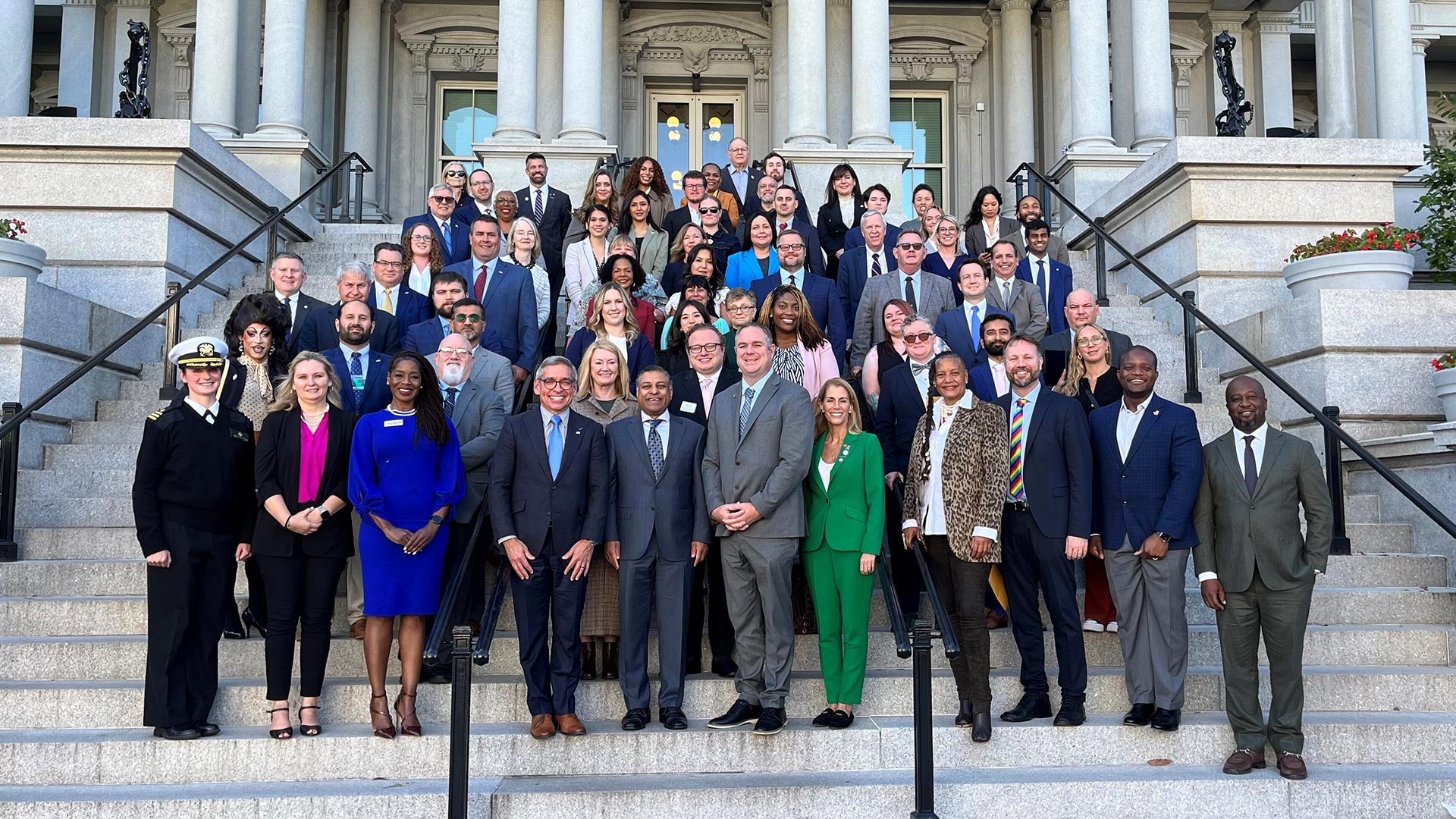 A group of people in business suits standing together on steps outside a legislative building.