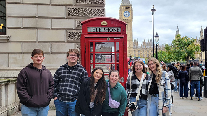 A group of young students posing for a photo in front of a red telephone booth, with Big Ben in the background.