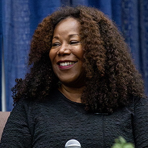 A black female with a dark top and a microphone.