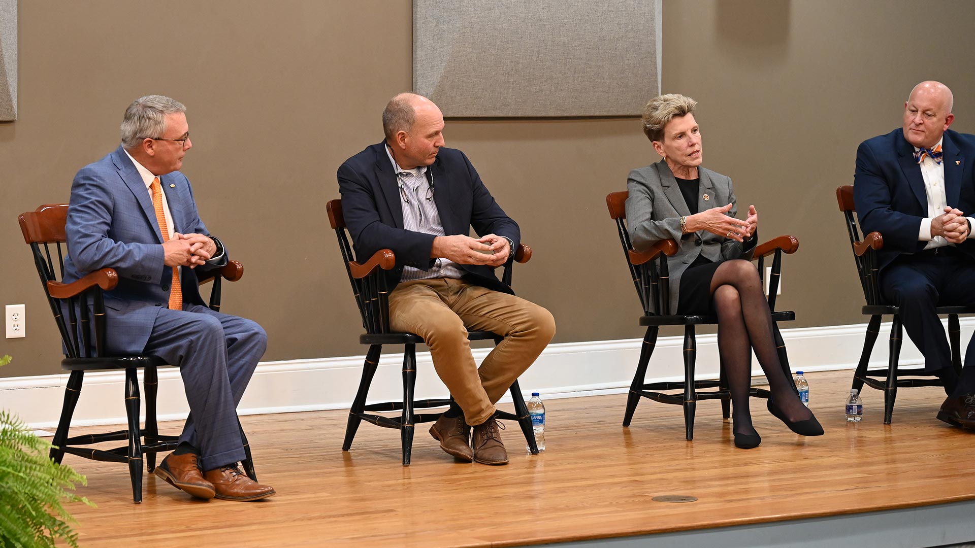 Three men and a woman, all wearing business attire, sit on stage during a panel discussion.