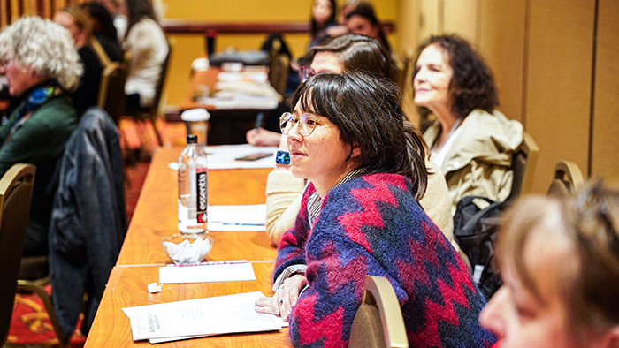 A group of people sitting at tables watching and listening to a presentation (off-image).