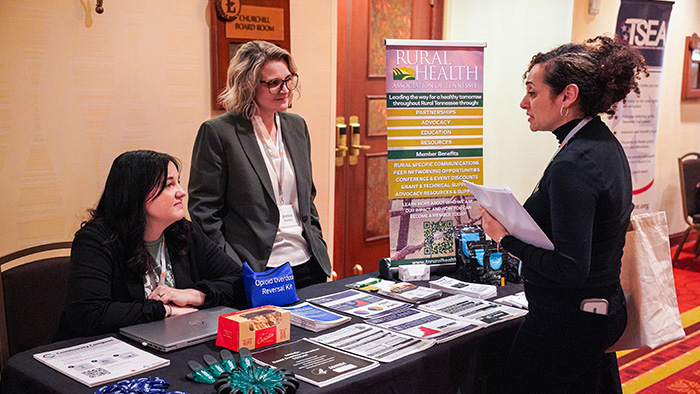 Three women talk around a table covered with display and handout materials.