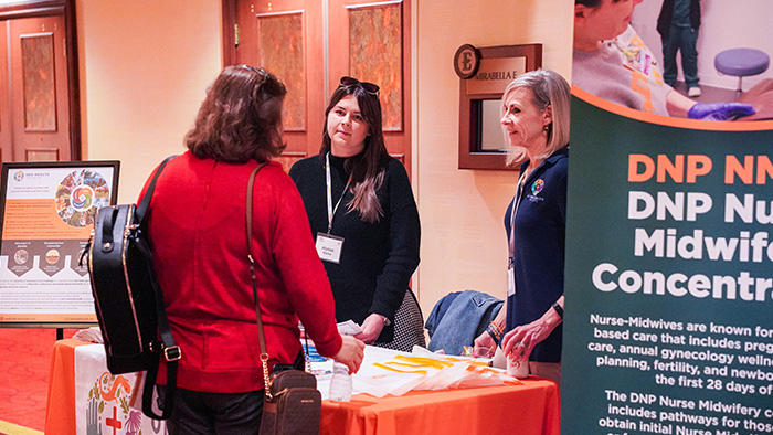 Three women talk around a table covered with display and handout materials.