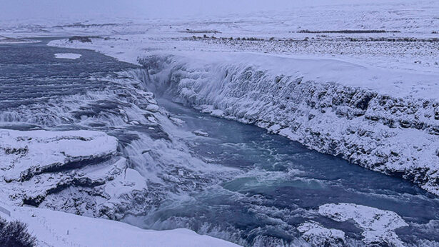 A flowing body of water in the middle of a frozen landscape in Iceland.