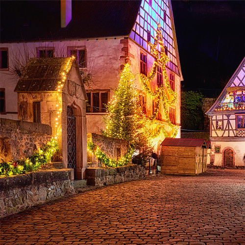 Old-town cobblestone street and houses lit up with christmas lights in the night.