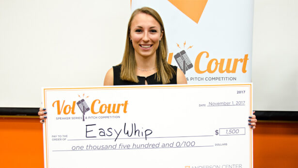 A white woman holds up an oversized award check.