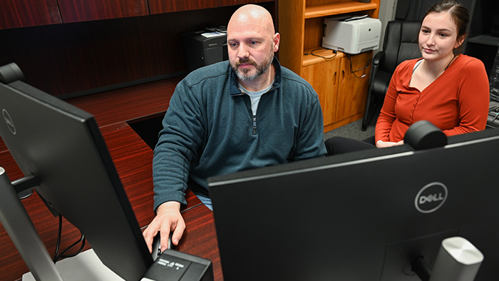 A man and woman looking at a pair of computer screens.