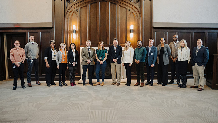 A large group of people in office attire pose for a photo inside of a fancy conference room.