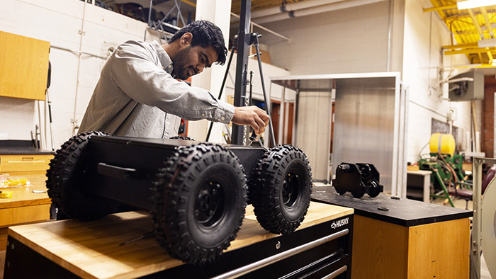 A man with black hair works on a large, wheeled robot in a workshop.