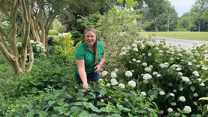 A blonde woman works in a lush flower bed.