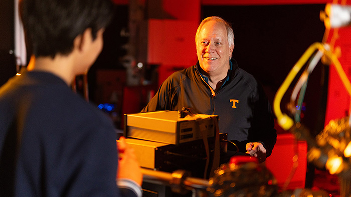 Two men wearing dark shirts work in a lab that is lit up with red and orange lighting.