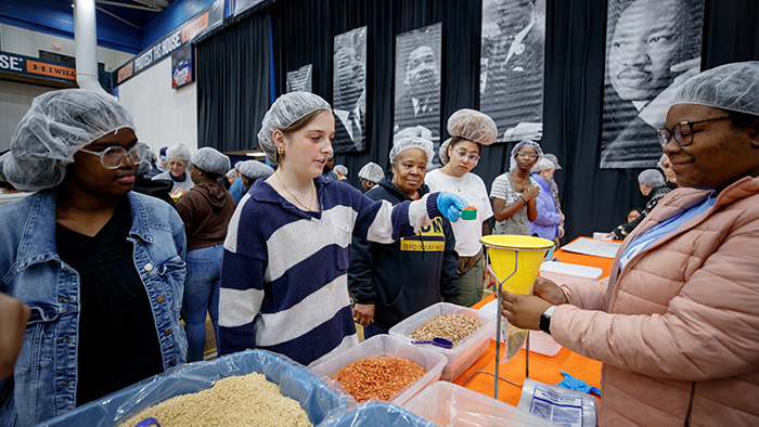 A group of volunteers wearing hair nets work to fill meal donations.