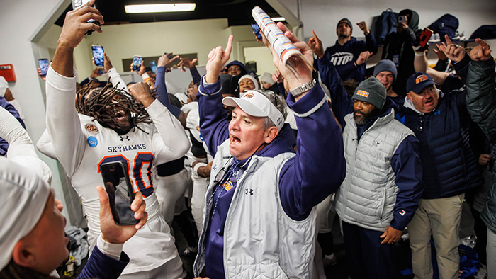 A group of student athletes and coaches celebrate in the locker room.