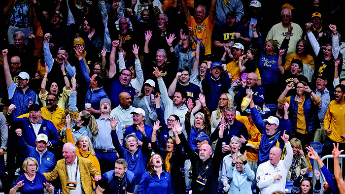 A large crowd of people in a basketball arena, all dressed in blue, white and gold outfits.