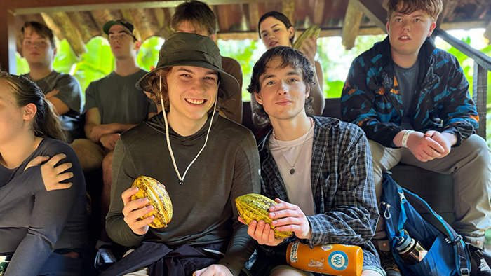 A group of students sitting in bleachers, holding up cacao plants.