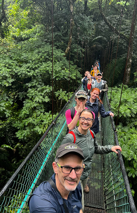 A group of people take a photo while on a suspended bridge in a rainforest.