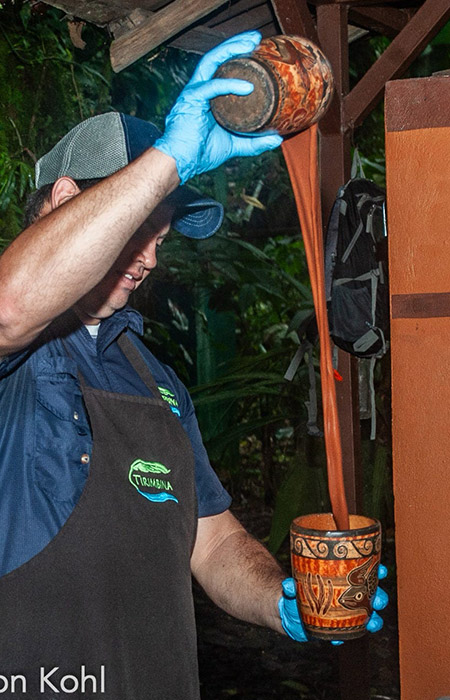 A man pours a long stream of freshly made chocolate into a decorated jar.