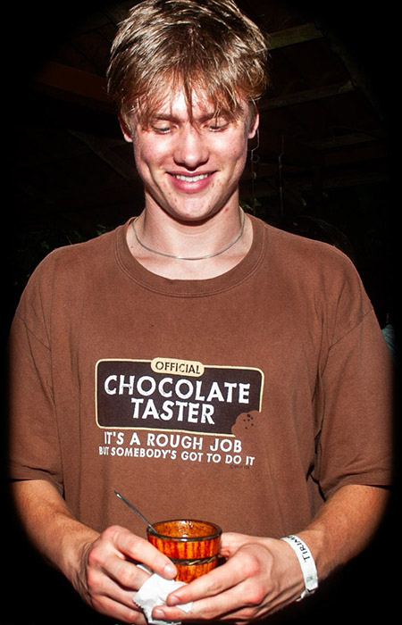 A male student in a brown shirt holds a cup of freshly made chocolate.