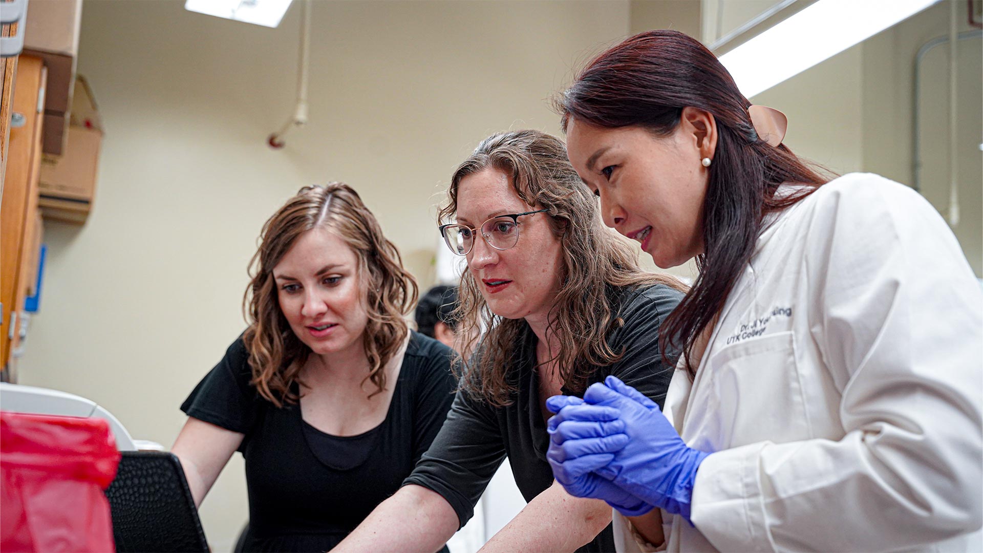 Three women look at a computer screen while working on a project in a laboratory.