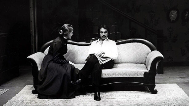 An old black and white photo of two people sitting on a couch as part of a theatre production.