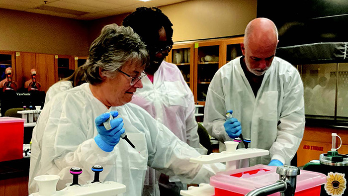 Three people wearing white lab coats working inside of a school laboratory.