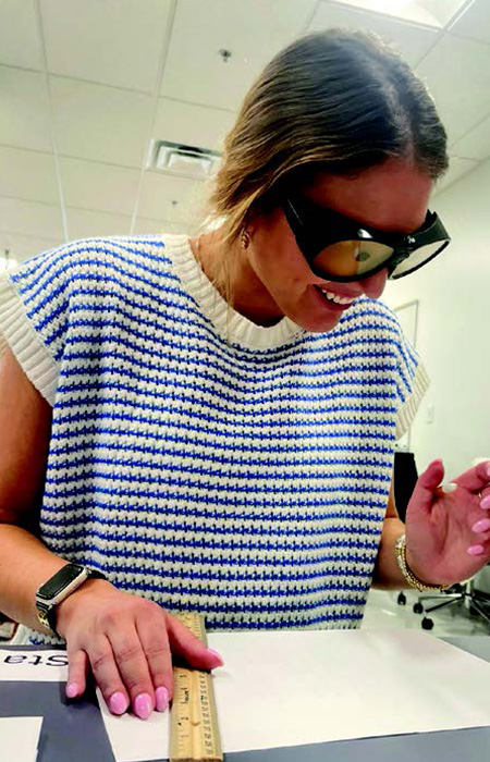 A woman in a white and blue striped shirt, wears goggles that simulate what vision with cataracts is like.
