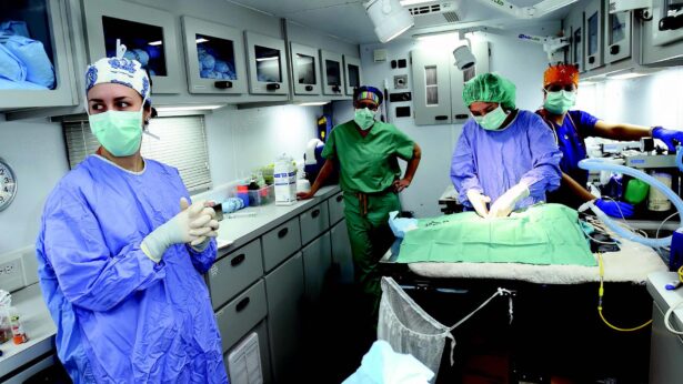 Four people wearing blue and green scrubs work inside a mobile medical center.