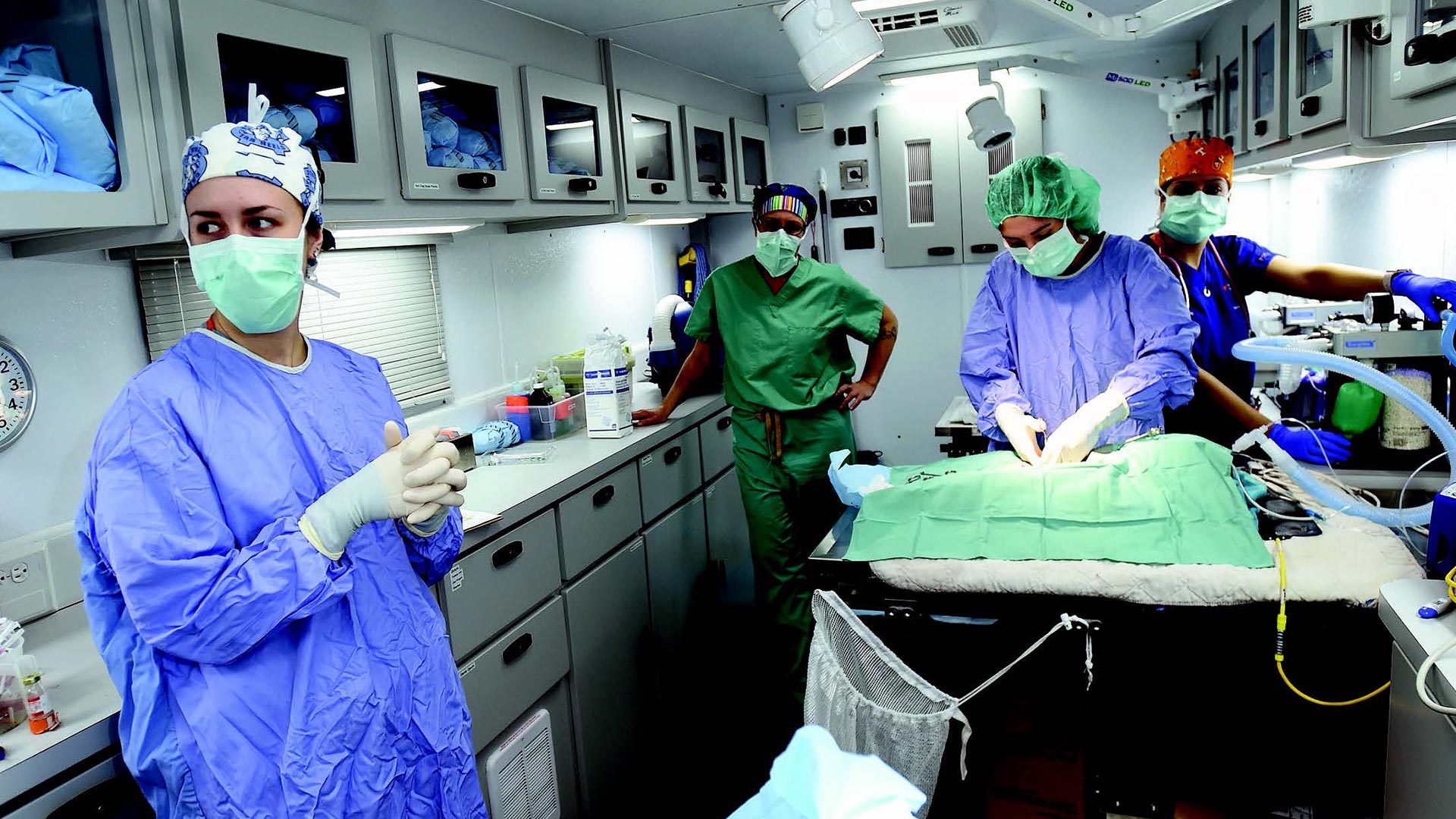 Four people wearing blue and green scrubs work inside a mobile medical center.
