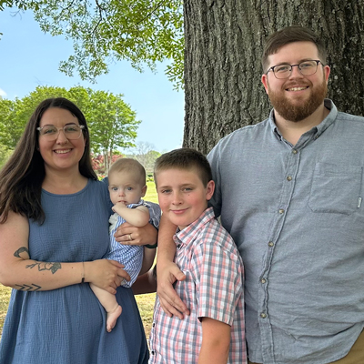 A family of four poses for a photo outside, in the shade of a tree.