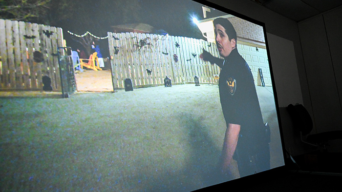 A large projected screen displays a video simulation for de-escalation training.