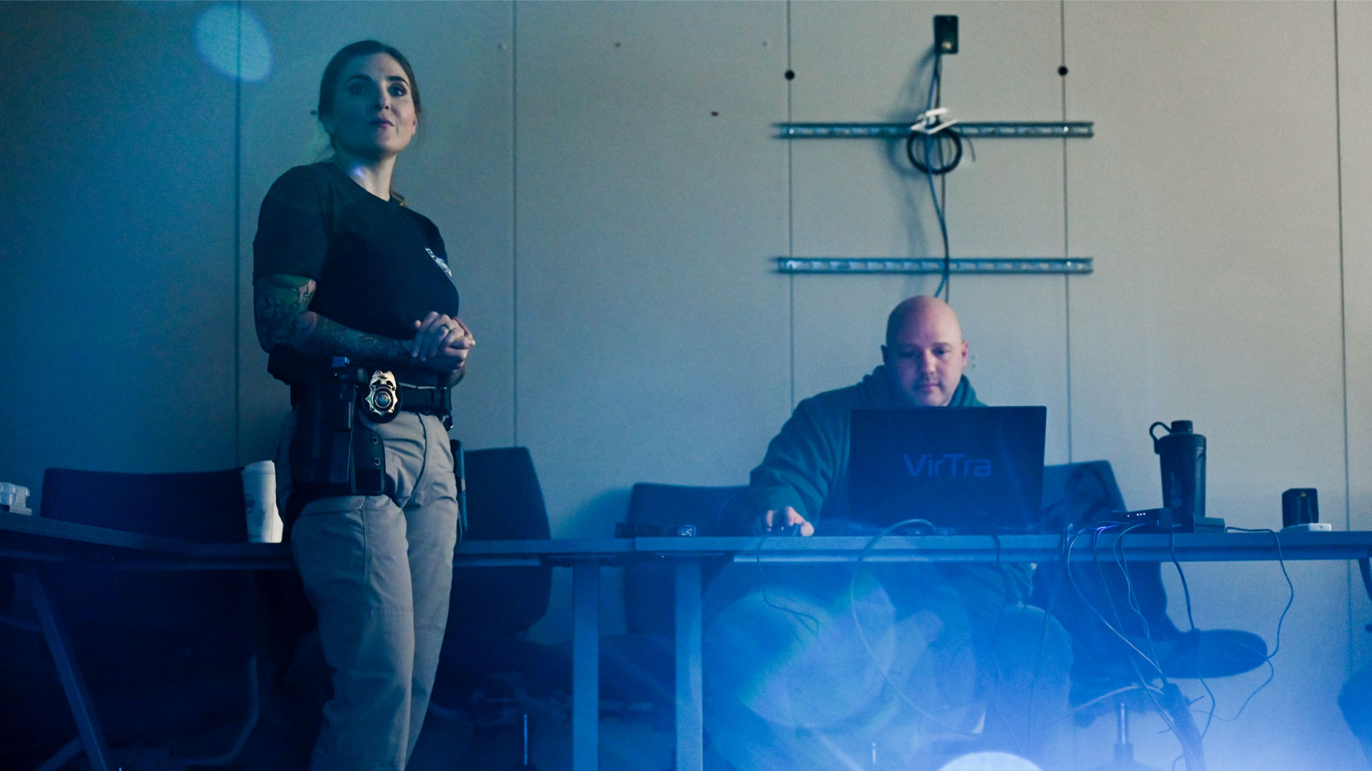 Two law enforcement officers sitting in a room, with a large projector screen.