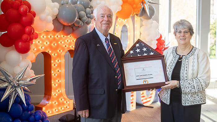 An older couple holding a framed, ceremonial plaque in front of a decorative backdrop.