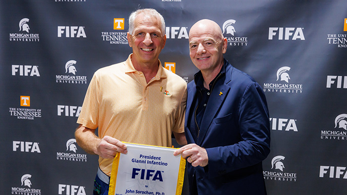 Two men holding a ceremonial cloth, marked with FIFA and UT Knoxville.