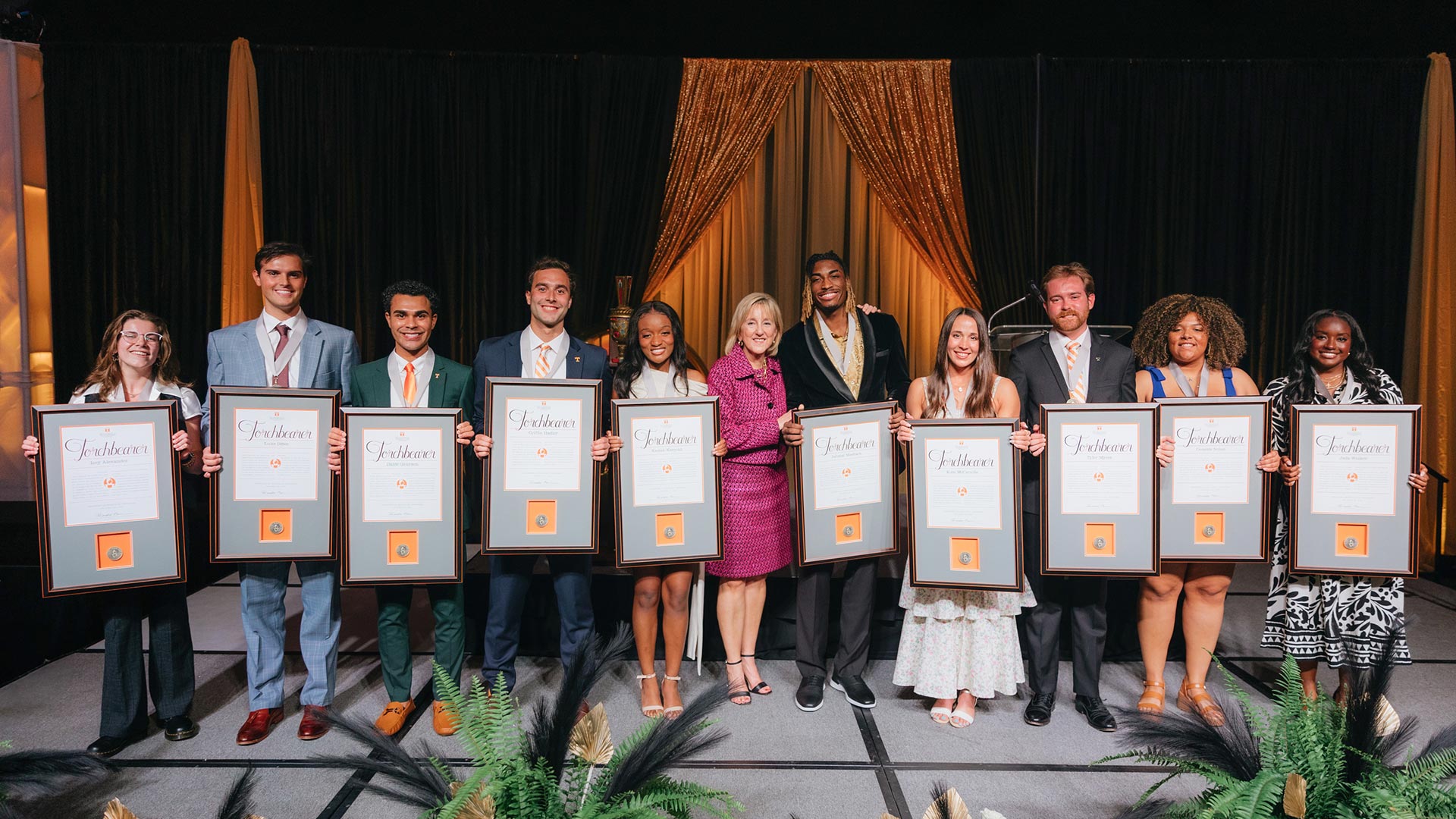 A diverse group of men and women standing on stage, each holding a framed plaque.