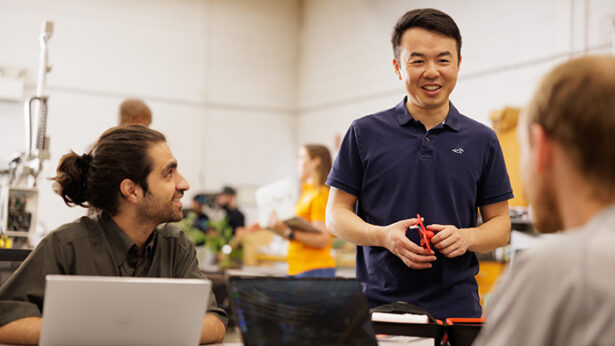 An asian man talks to two other men inside a classroom.