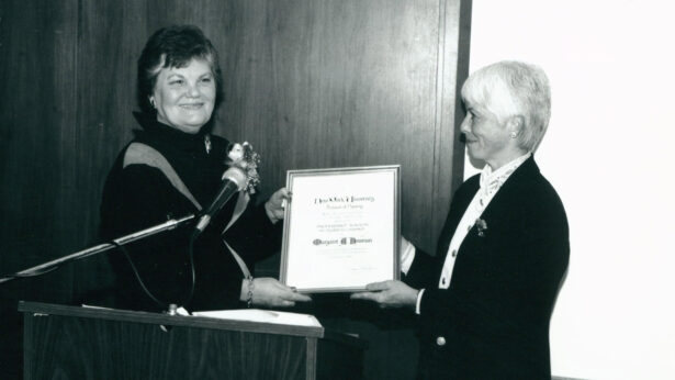 A historic, black and white photo of two women holding an award during a ceremony.