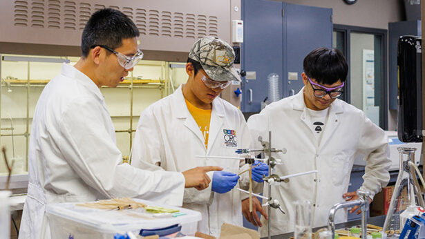Three asian men wearing lab coats, while working on an experiment inside of a laboratory.