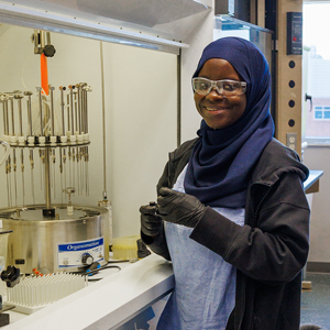 A black woman, wearing a hijab, working on an experiment inside of a laboratory.