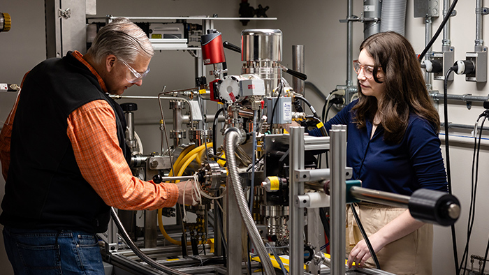 A man and woman work on a large, complicated piece of machinery.