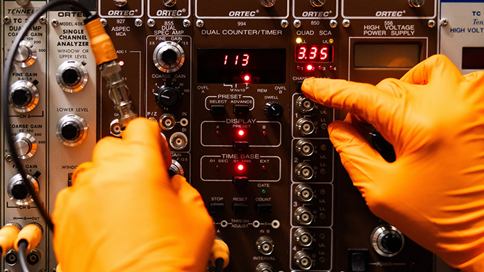 A person wearing orange gloves, operates a complicated machinery display.