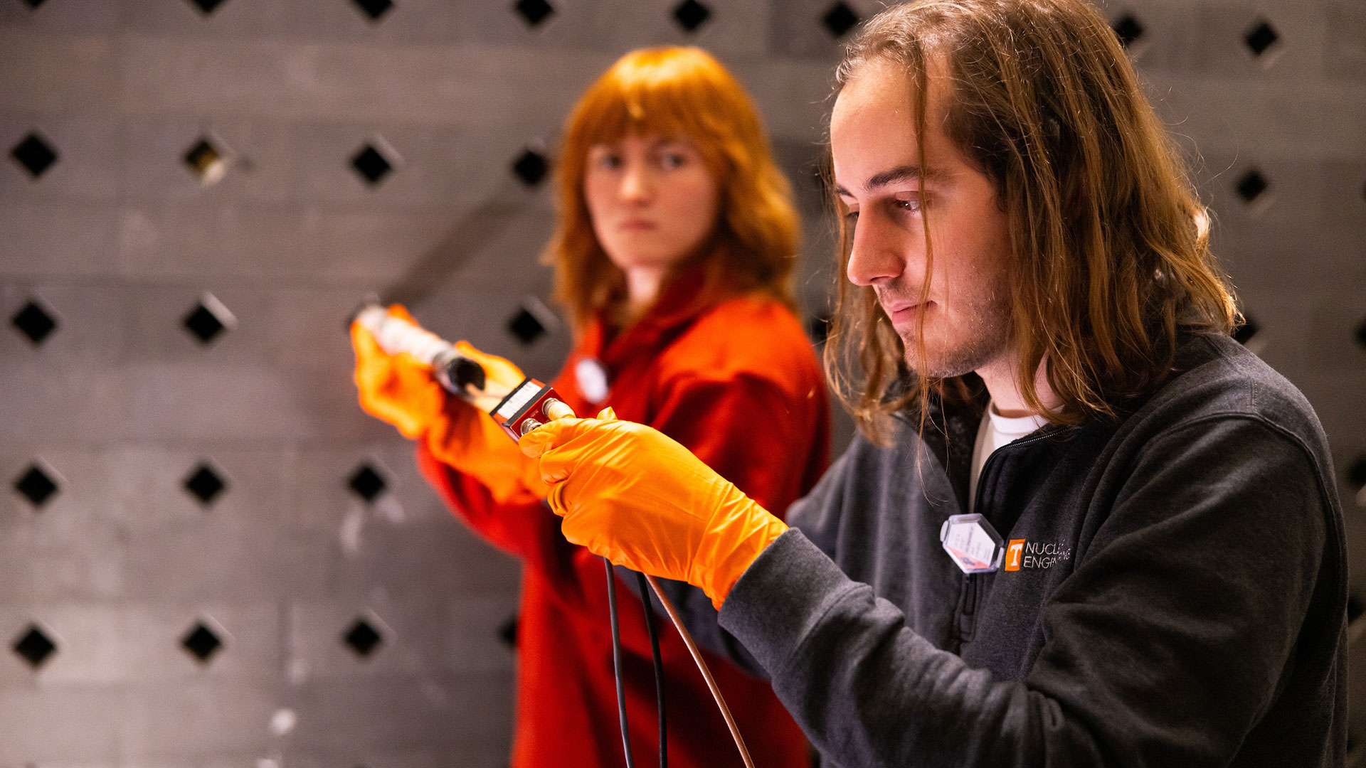 Two students work together to operate and examine a long piece of equipment.