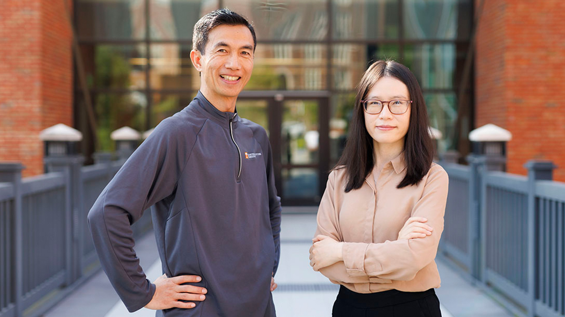 An asian man and woman pose for a photo in front of a brick building.