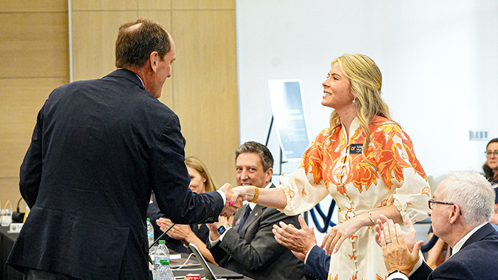 A blonde, female student shakes hand with a man in a business suit.