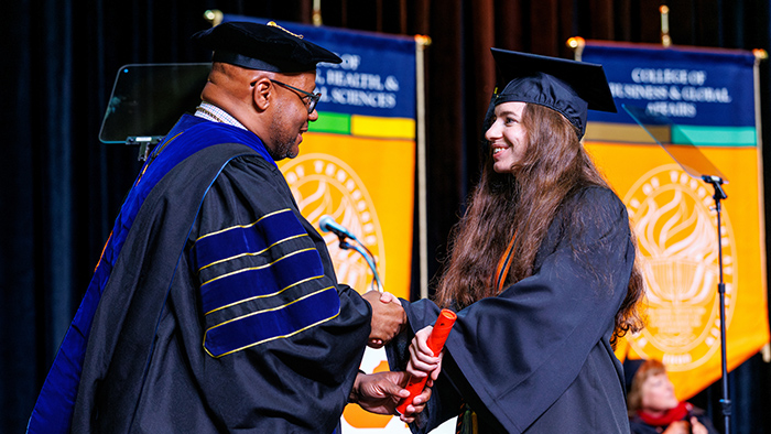 A young woman receives her college diploma from a black man during a graduation ceremony.