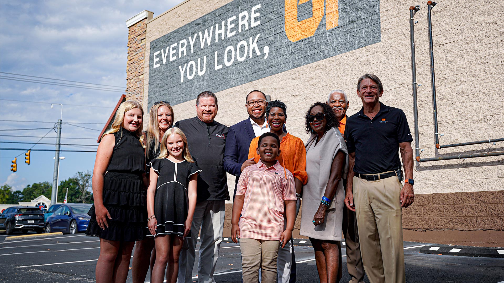 A group of people stand next to a building with a new "Everywhere You Look, UT" mural painted on it.