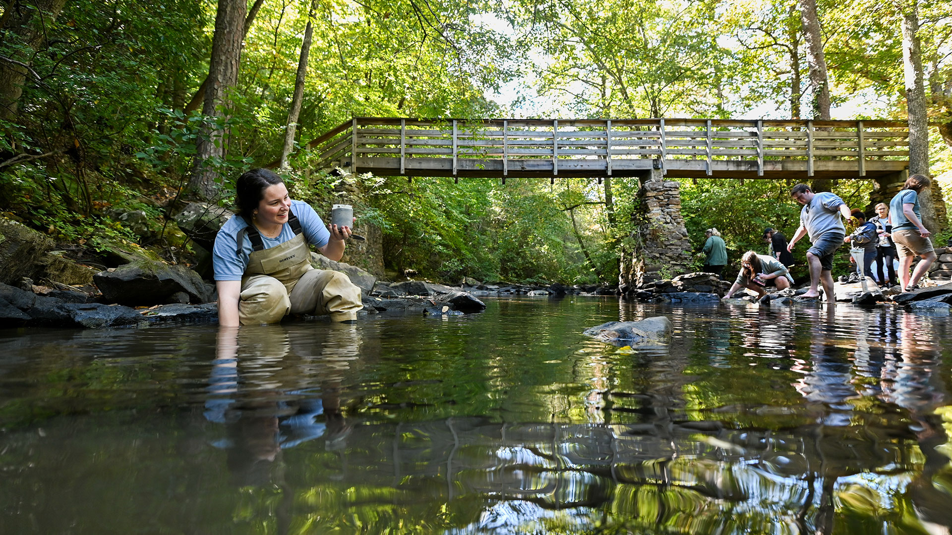 A group of people examining and collecting samples from a creek bed.